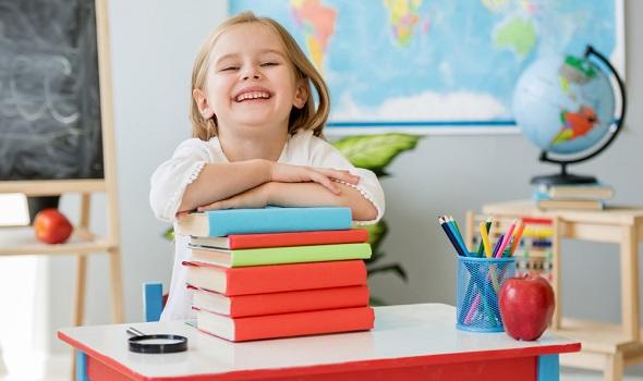 Namensetiketten_Freepik_little-smiling-blond-girl-sitting-at-the-white-desk-and-holding-hands_tan4ikk.jpg