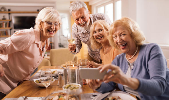 group-of-happy-seniors-using-smart-phone-and-taking-selfie-at-dining-table-at-home.jpeg